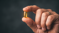 Hand holding a single golden softgel